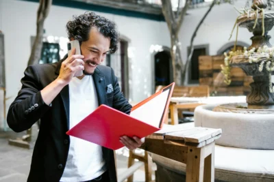 Happy man talking on phone and looking at red binder. Unsplash+